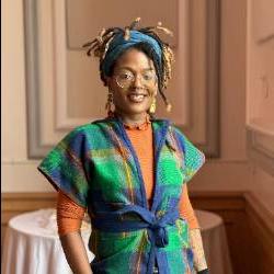 a headshot of an artist with dreads wearing a colorful vest